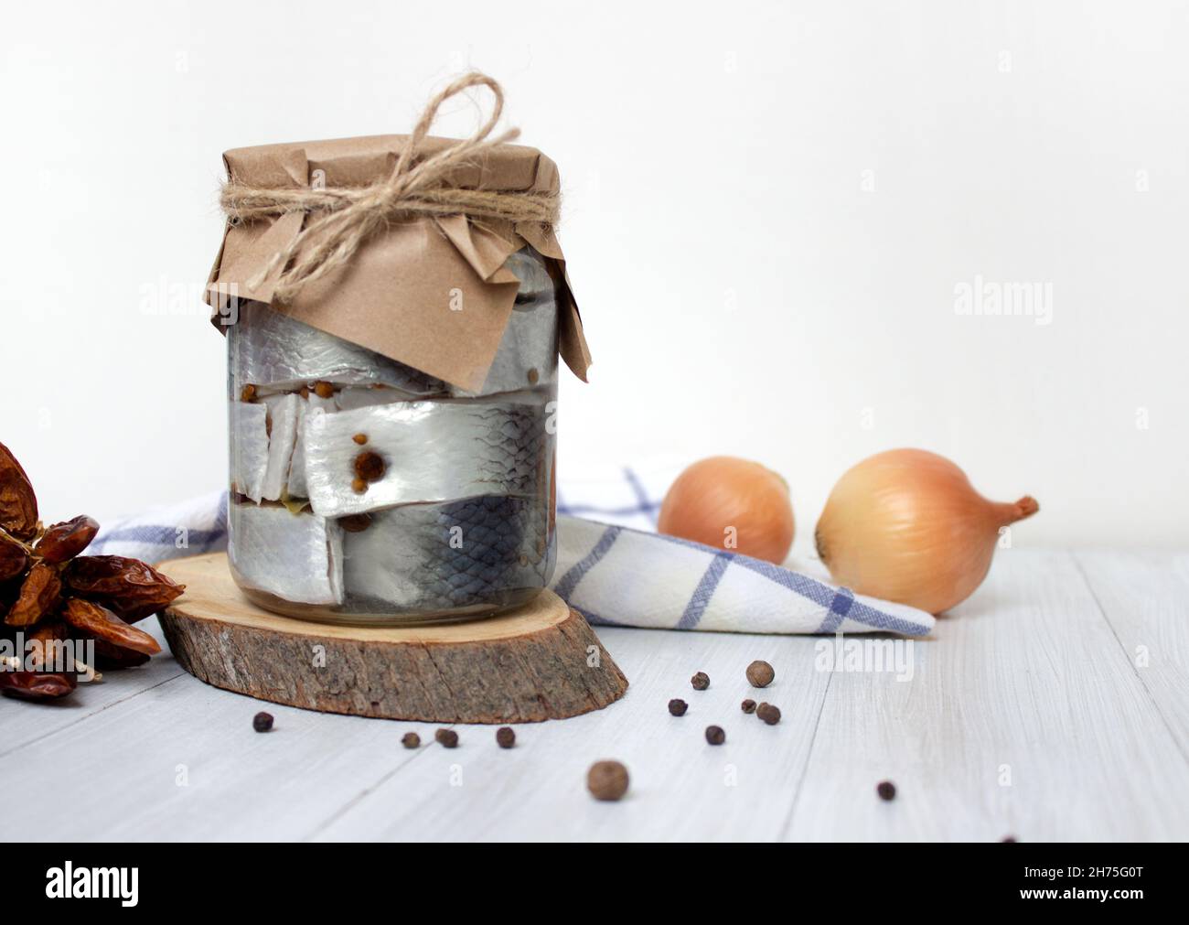 Pickled herring fish with pepper in jar on the table on light