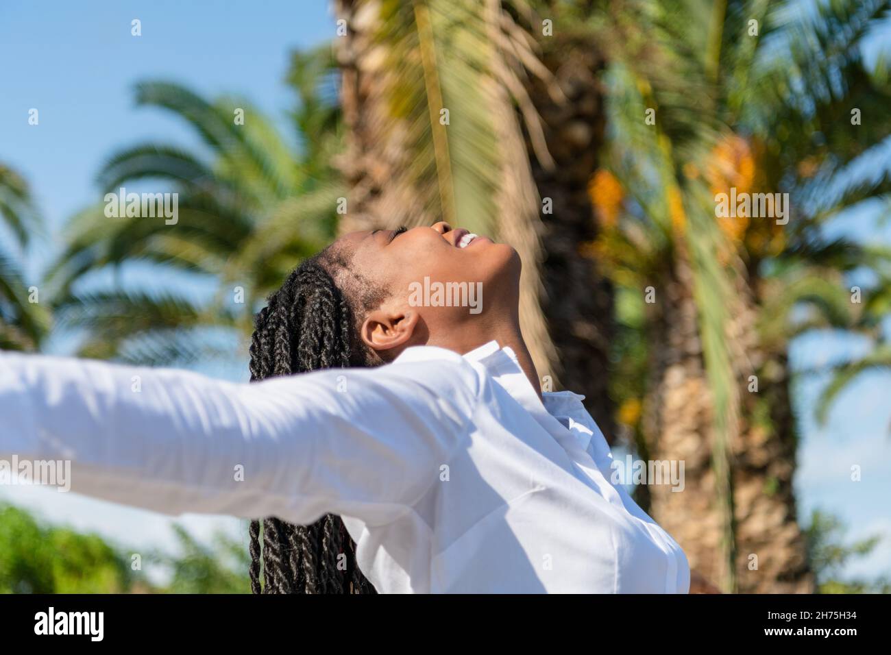 Happy african woman raising arms while facing the sun in a park Stock ...