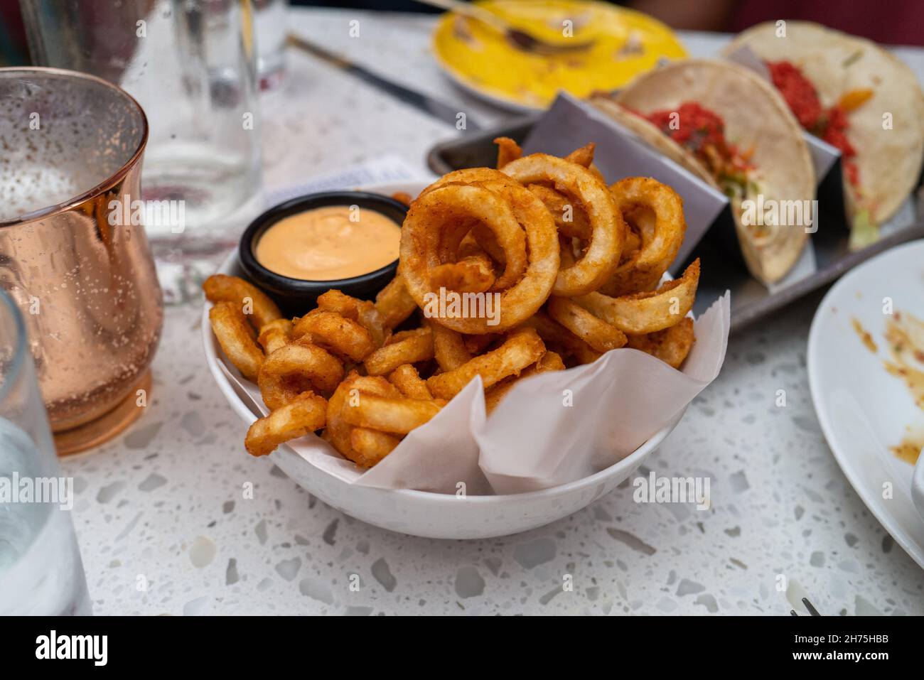 Curley Fries in a white bowl with Chipotle Sauce with tacos in the background Stock Photo