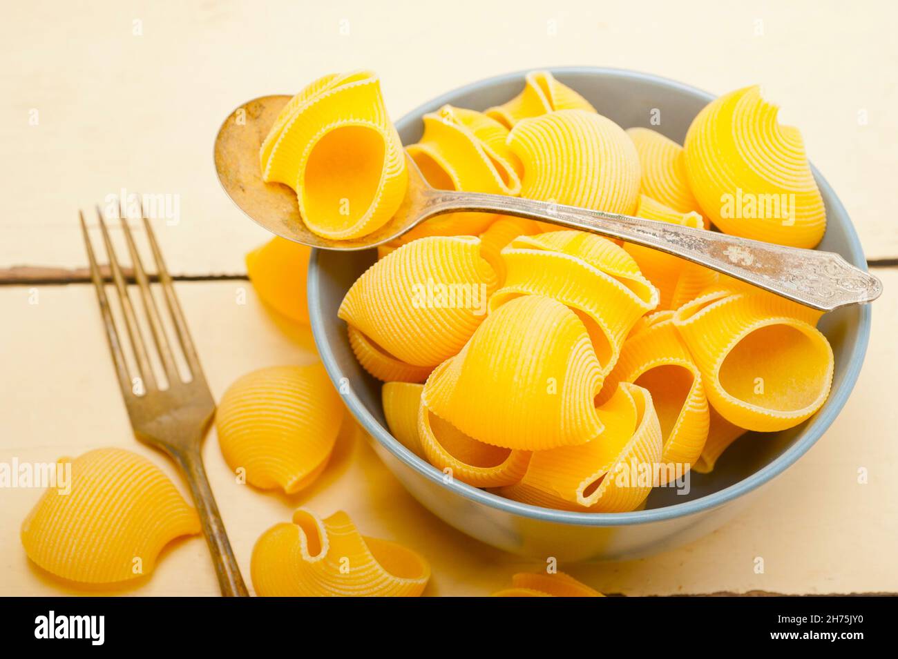 raw Italian snail lumaconi pasta on a blue bowl over rustic table macro Stock Photo