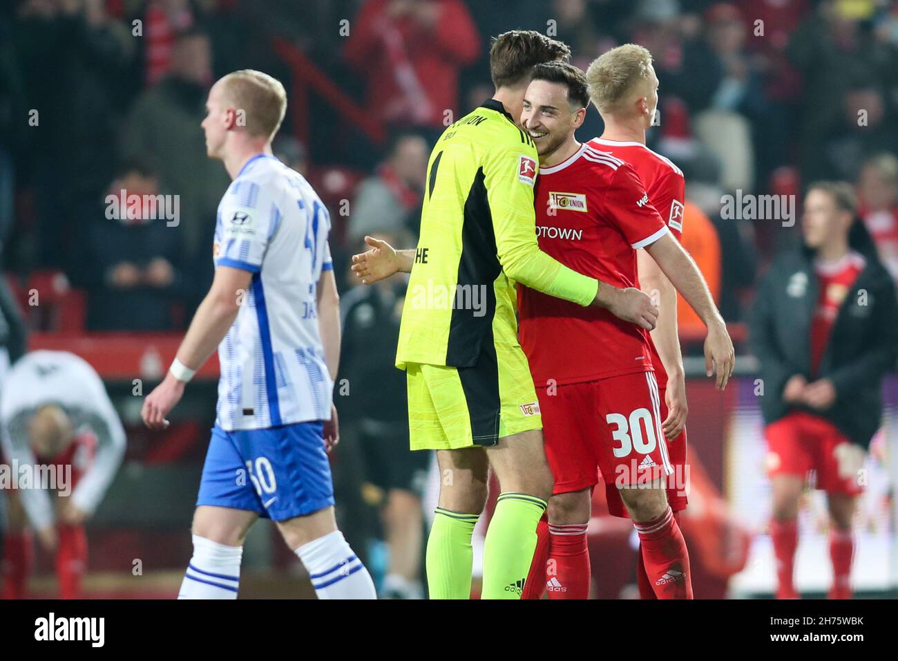 20 November 2021, Berlin: Football: Bundesliga, 1. FC Union Berlin - Hertha BSC, Matchday 12, at the stadium 'An der Alten Försterei'. Union Berlin's Kevin Möhwald (r-l) cheers with Union Berlin's goalkeeper Andreas Luthe after the match, while Hertha's Dennis Jastrzembski walks past them. IMPORTANT NOTE: In accordance with the regulations of the DFL Deutsche Fußball Liga and the DFB Deutscher Fußball-Bund, it is forbidden to exploit or have exploited photographs taken in the stadium and/or of the match in the form of sequence pictures and/or video-like photo series. Photo: Andreas Gora/dpa - Stock Photo