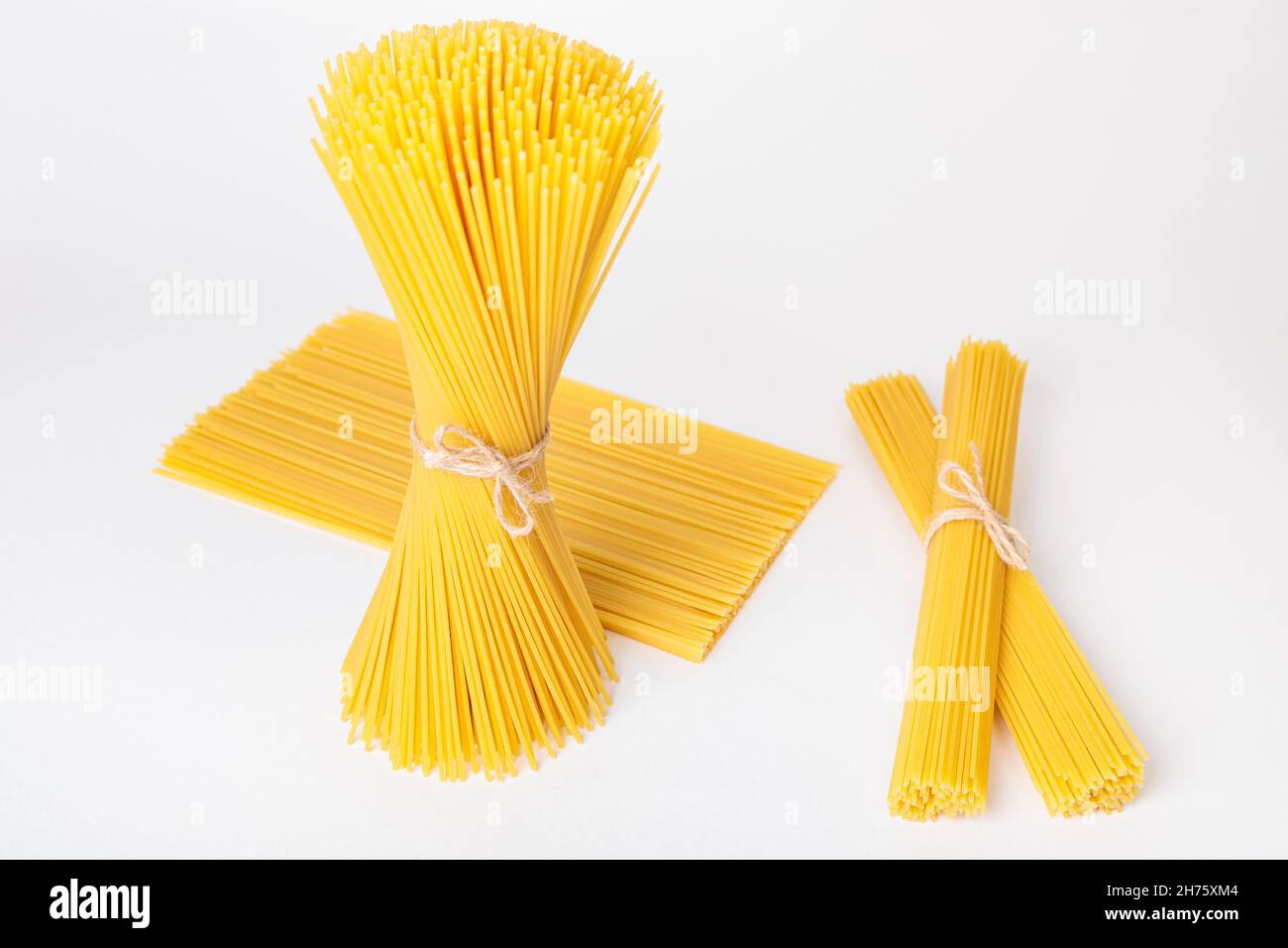 Set of bundles of raw spaghetti, tied with thread, on a white ...