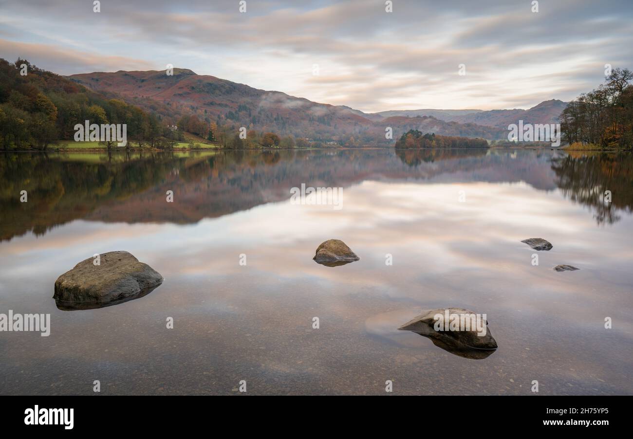 A wide shot of Grasmere captured from the beach at the bottom of the lake with the island and shoreline perfectly mirrored in the calm waters. Stock Photo