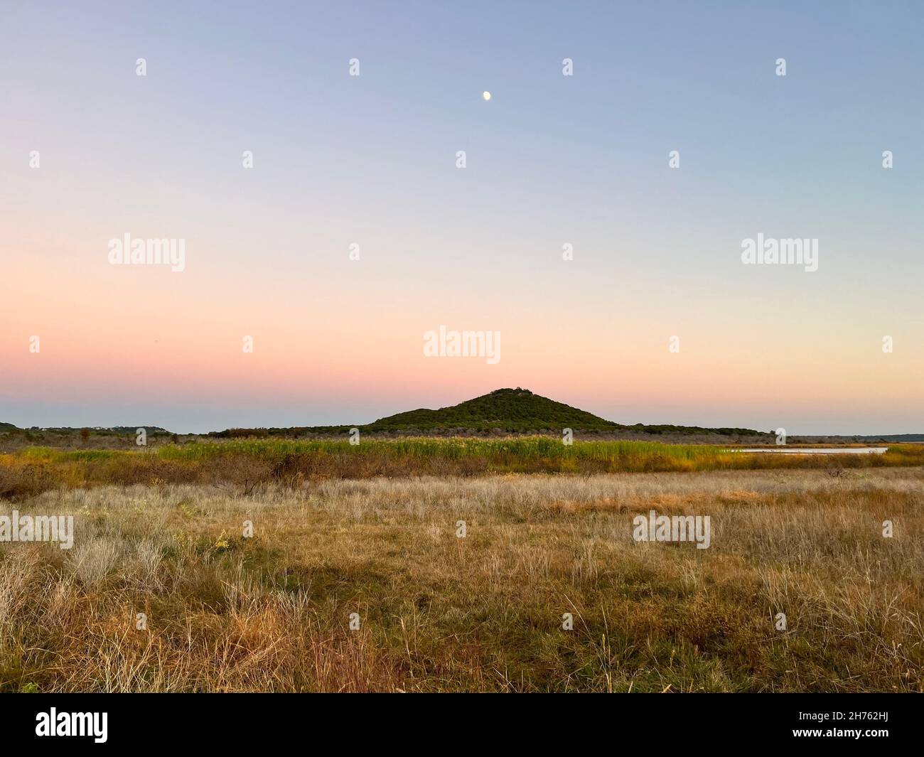 The magical colorful twilight sky as the moon rises over the mountain top horizon the crisp cool breeze blows across the grassy tundra in Texas. Stock Photo