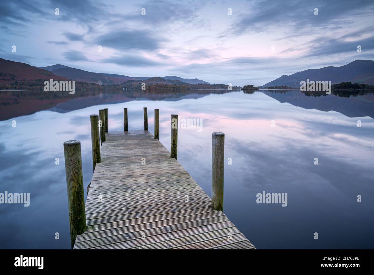 The famous Ashness Jetty on Derwentwater leads the eye towards the perfectly reflected fells surrounding the lake on a perfectly calm autumn morning. Stock Photo