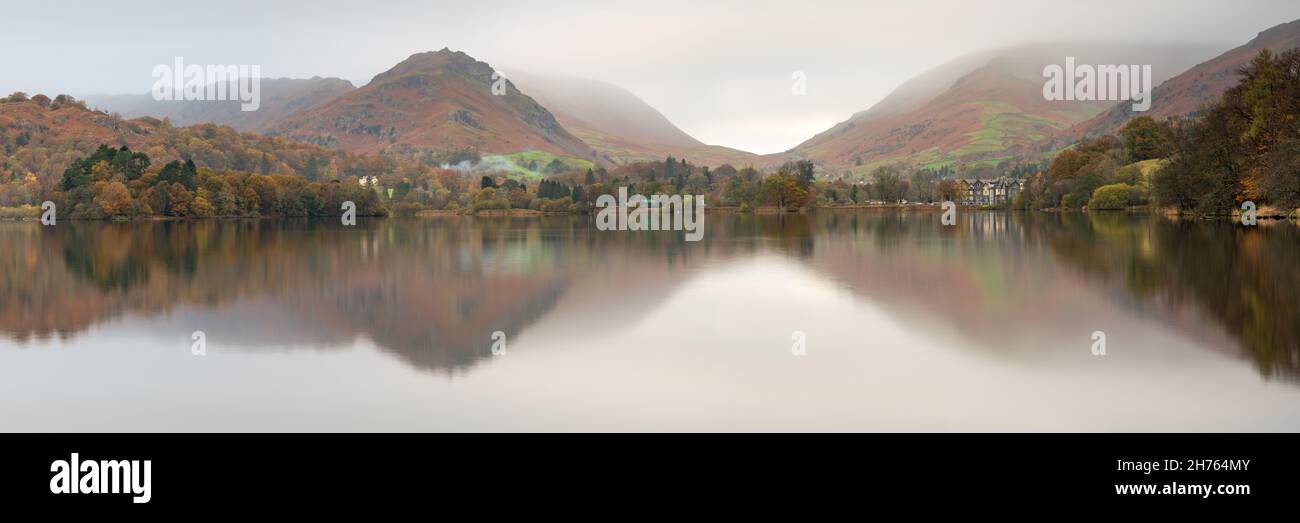 An autumnal panoramic reflection of Grasmere and the surrounding fells on an atmospheric day of low cloud in the Lake District National Park. Stock Photo