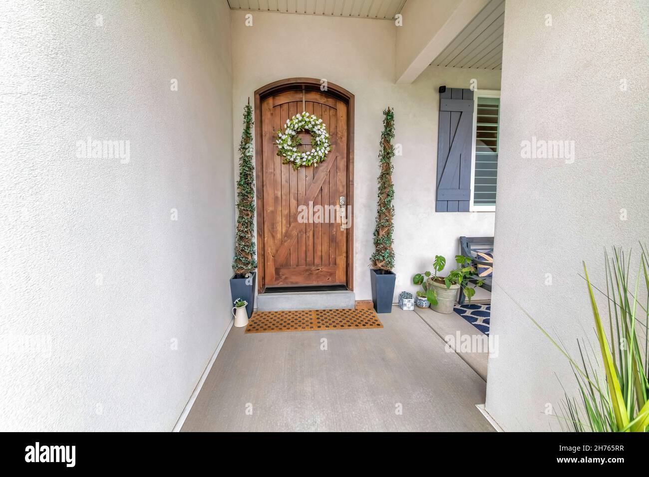 Arched wooden door with digital entry access, wreath and topiary spiral shrubs Stock Photo