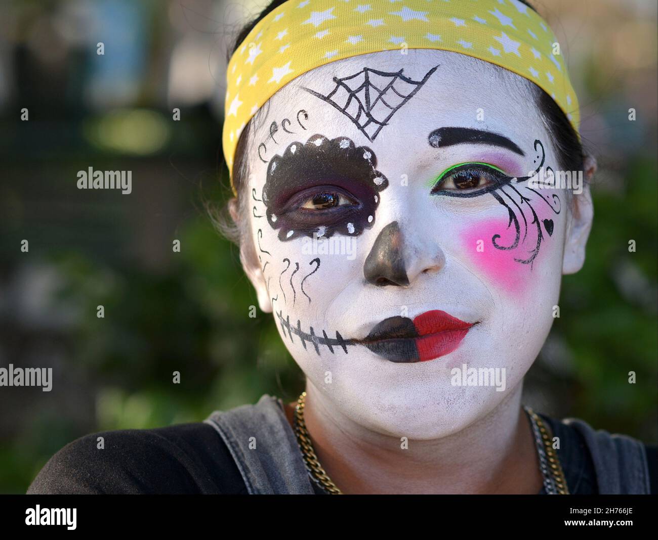 Young Mexican artist with dual catrina and clown face paintings (death and life) on the Day of the Dead (Día de los Muertos) looks at the viewer. Stock Photo