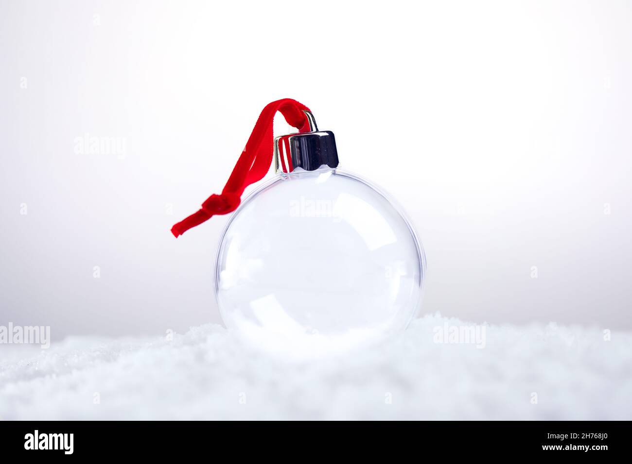 Clear empty Christmas ornament with red ribbon sitting in snow Stock Photo