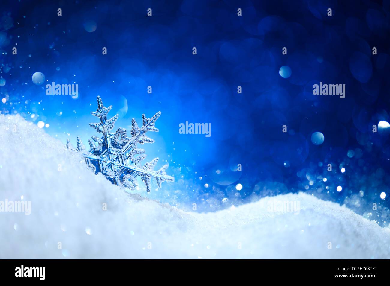 Snowflake on glittering white snow with sparkling blue background. Stock Photo