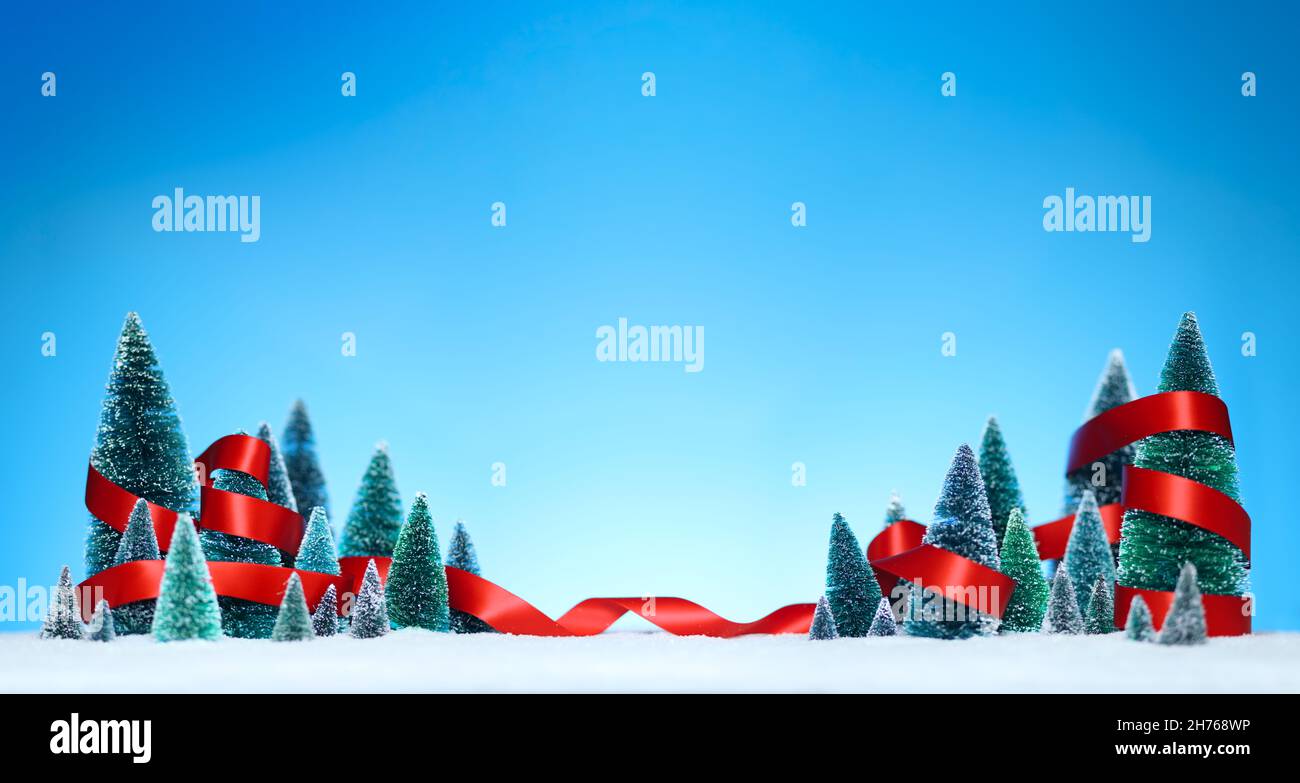 Winter wonderland with miniature tree decorations wrapped in a shiny red ribbon on sparkling snow. Stock Photo