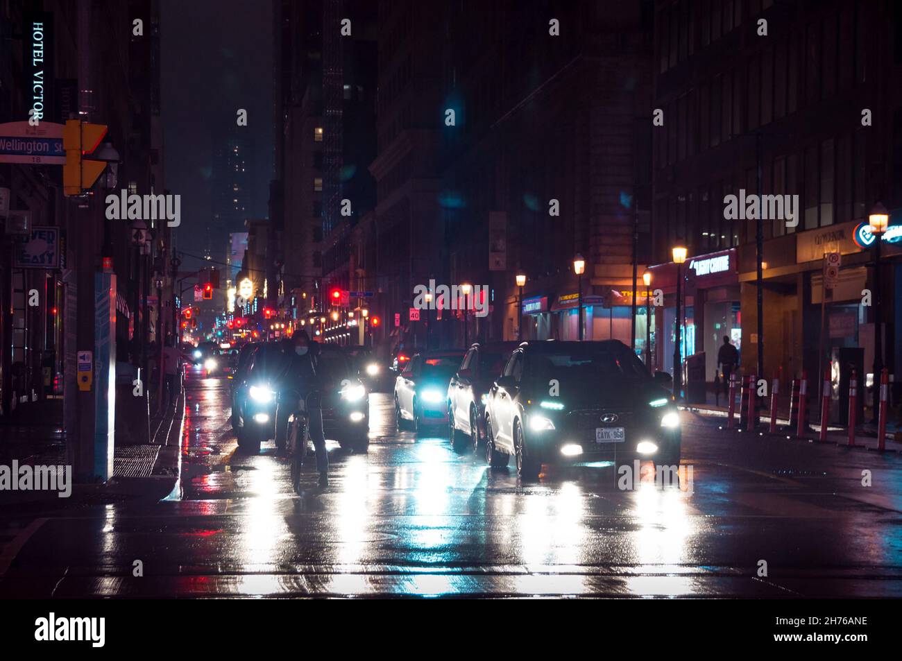 Toronto, Canada - 10 30 2021: Rainy night view along Yonge street from Wellington street in downtown Toronto with a cyclist in a mask, cars waiting fo Stock Photo