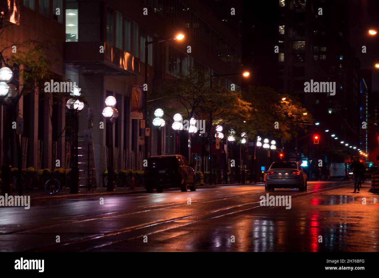Rainy night view along a city street with a line of street lamps, cars ...