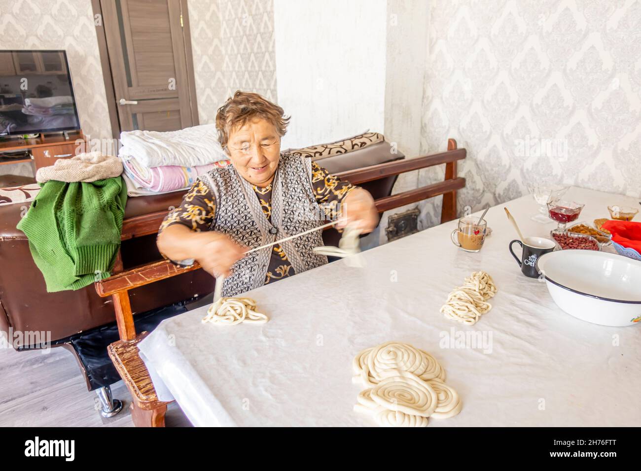 An elderly kazakh woman preparing pooled long noodles for cooking laghman dish- a traditional Central Asian meal Stock Photo