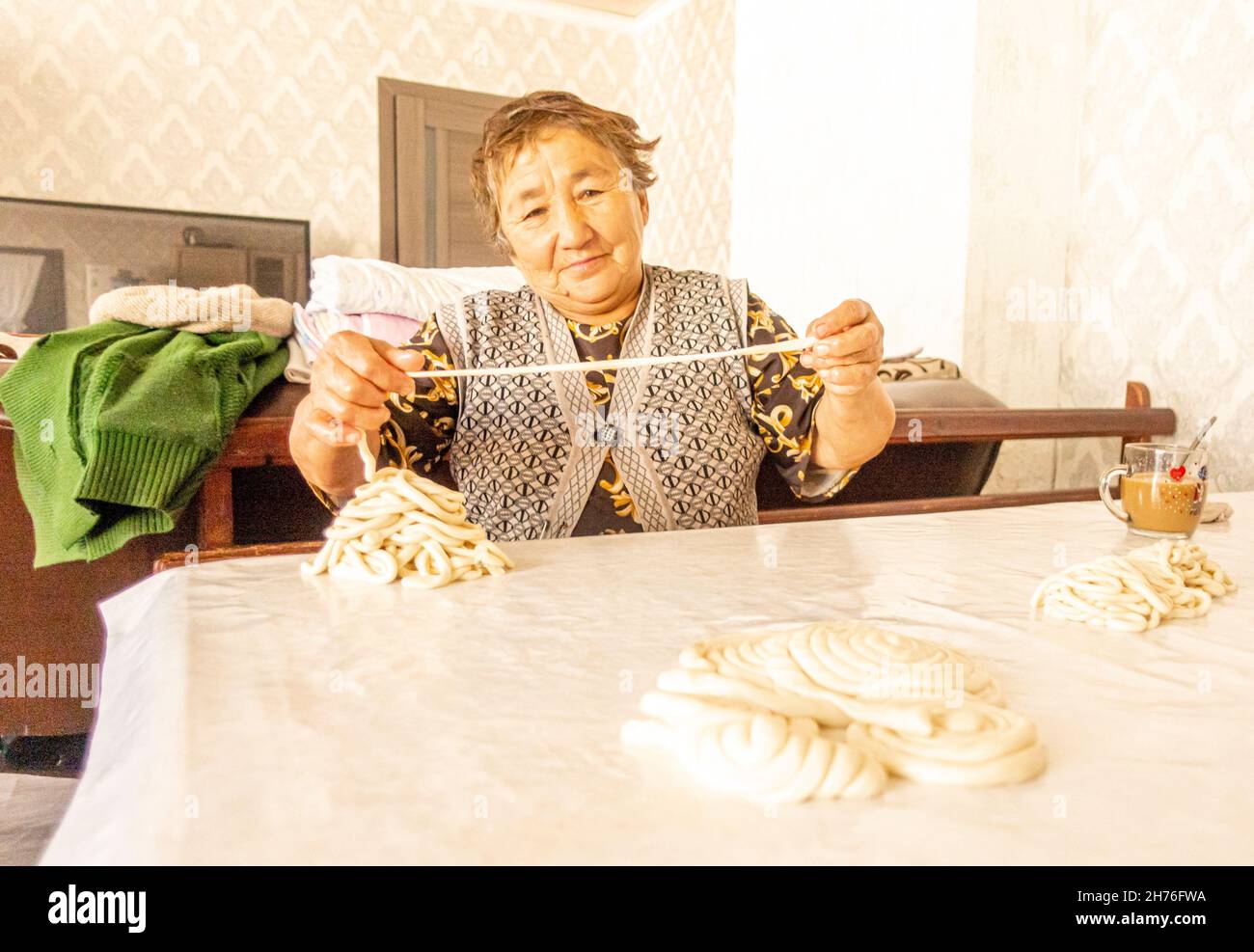 An elderly kazakh woman preparing pooled long noodles for cooking laghman dish- a traditional Central Asian meal Stock Photo