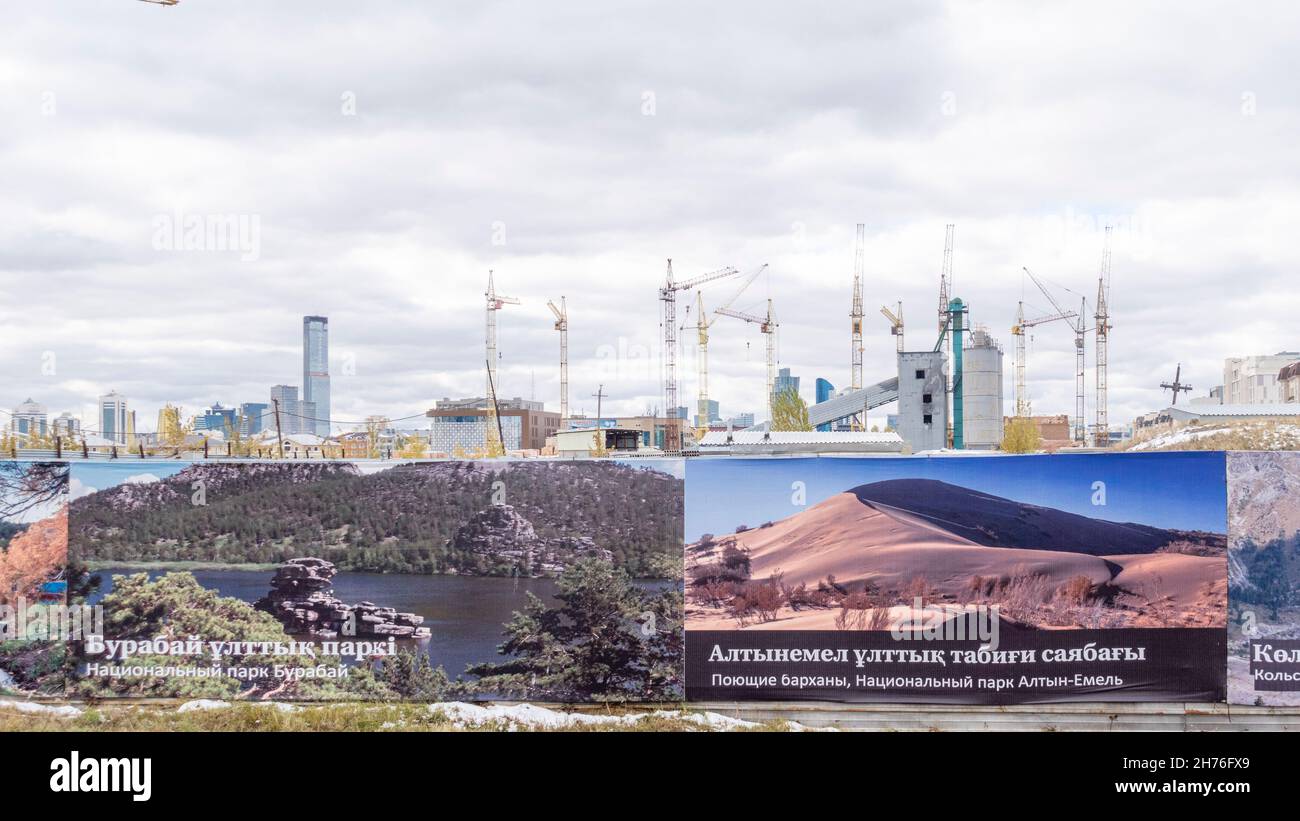 Massive construction site with cranes at real estate development area in Nur-Sultan, Kazakhstan. Billboards advertising travel landmarks as a fence. Stock Photo