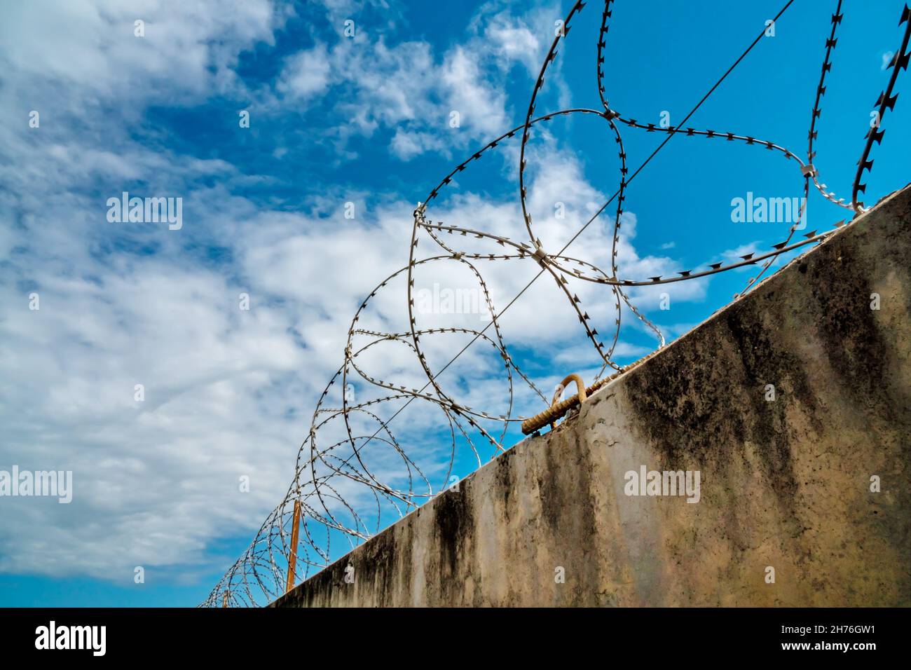 Old moldy concrete fence with barbed wire from above against the beautiful sky. Stock Photo