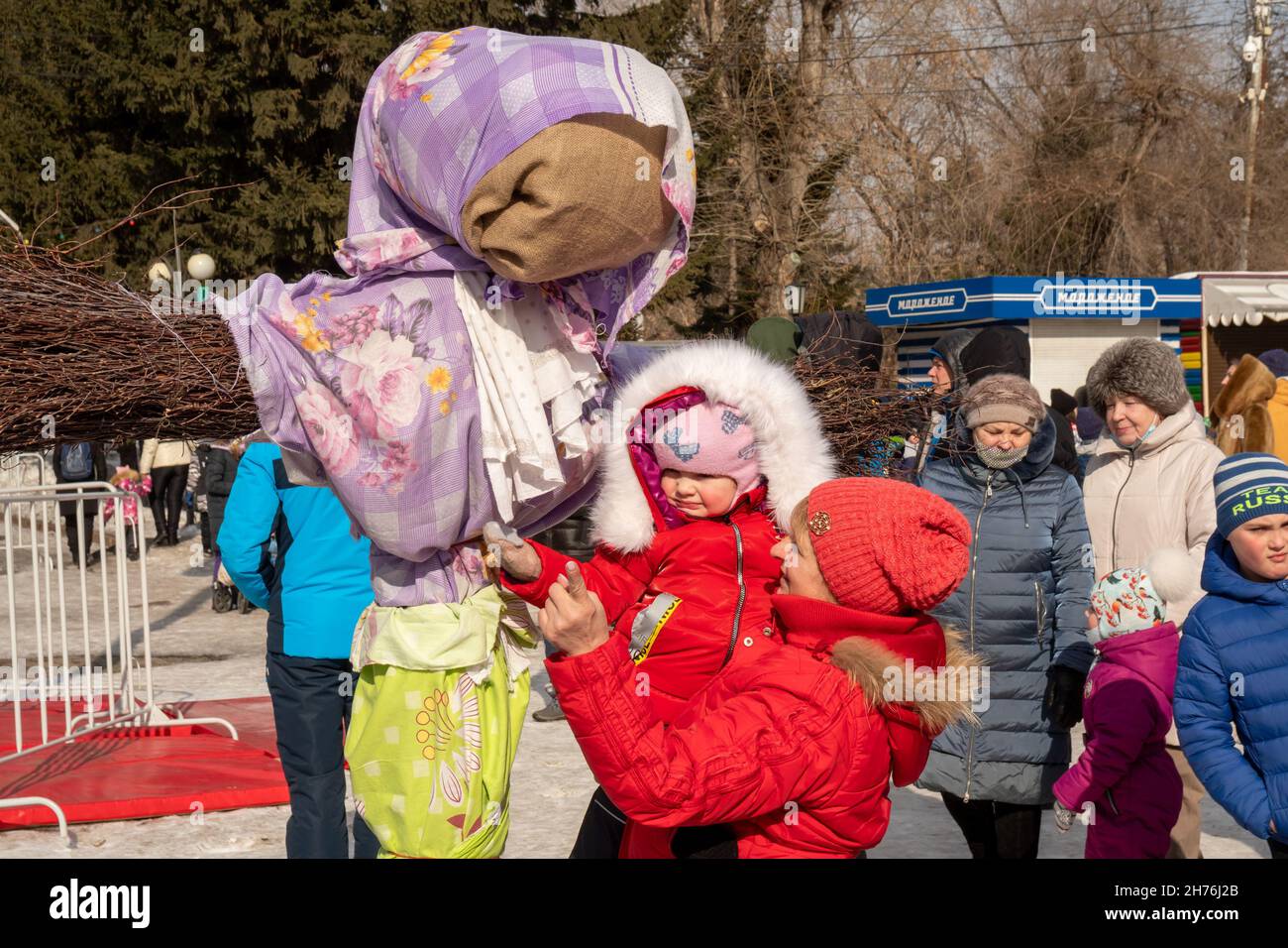 A mother with a child in her arms stands near a stuffed Shrovetide at the holiday Seeing off the winter among a crowd of people. Stock Photo