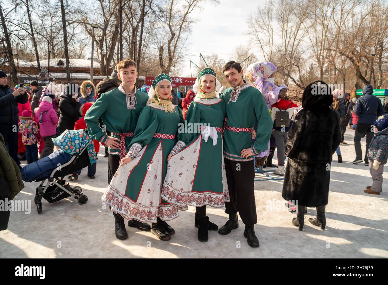 Happy young people in Russian ethnic costumes stand among the crowd of people at the Happy Winter holiday in the city park. Stock Photo