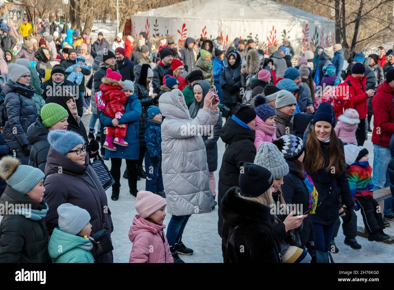Woman taking pictures on the phone while standing among the crowd of people at the Farewell to Winter holiday in the city park. Stock Photo