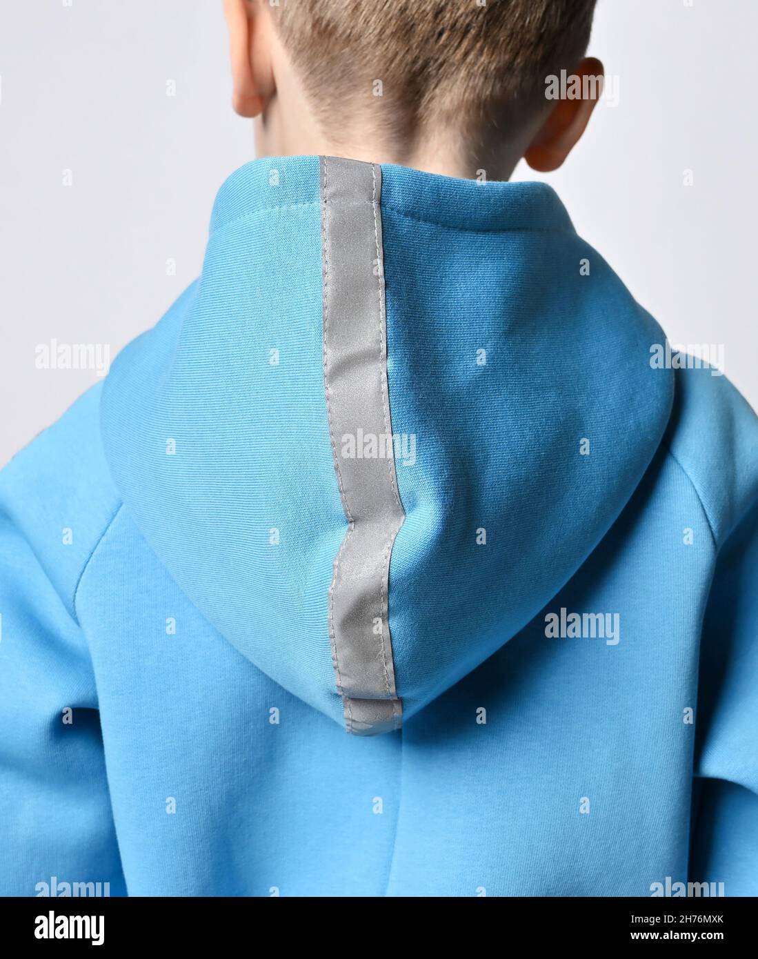 Closeup of kid boy in blue jumpsuit or hoodie standing back to camera. Shoulders, cowl with retroreflective strip Stock Photo