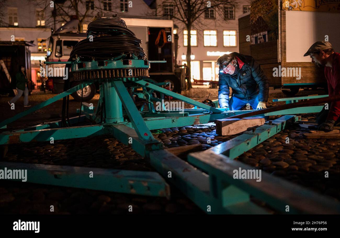 20 November 2021, Lower Saxony, Lüneburg: Showmen are setting up a carousel for the Christmas market on the town hall square. The smell of bratwurst and almonds should attract visitors to Lüneburg's old town from Wednesday (24 November) onwards. By setting up the stalls, the Hanseatic city wants to implement the concept of Lüneburg as a Christmas city. The 2G rule is to be applied. Photo: Philipp Schulze/dpa Stock Photo