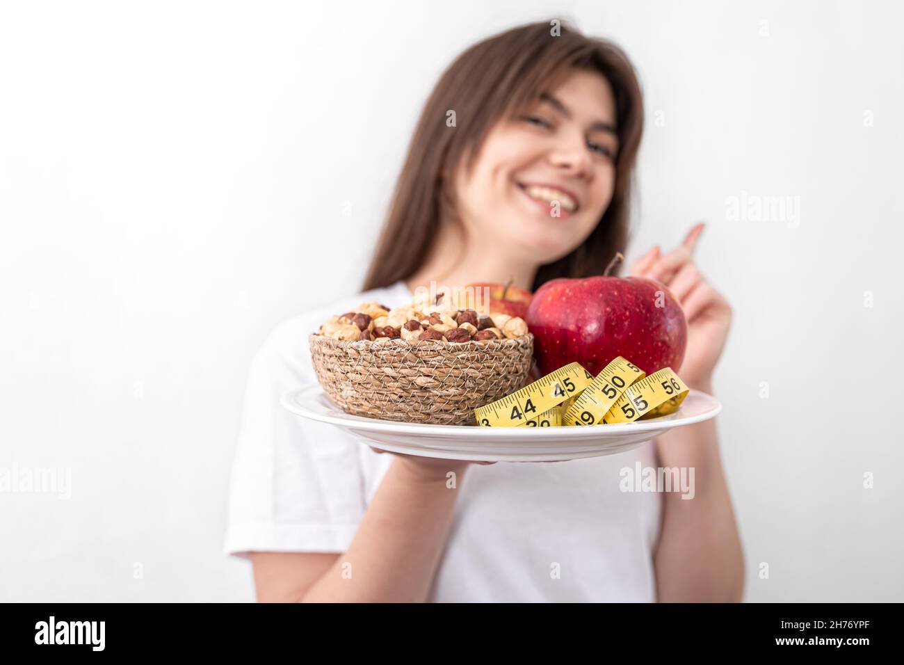 A plate with apples, nuts and a measuring tape in the hands of a young woman. Stock Photo
