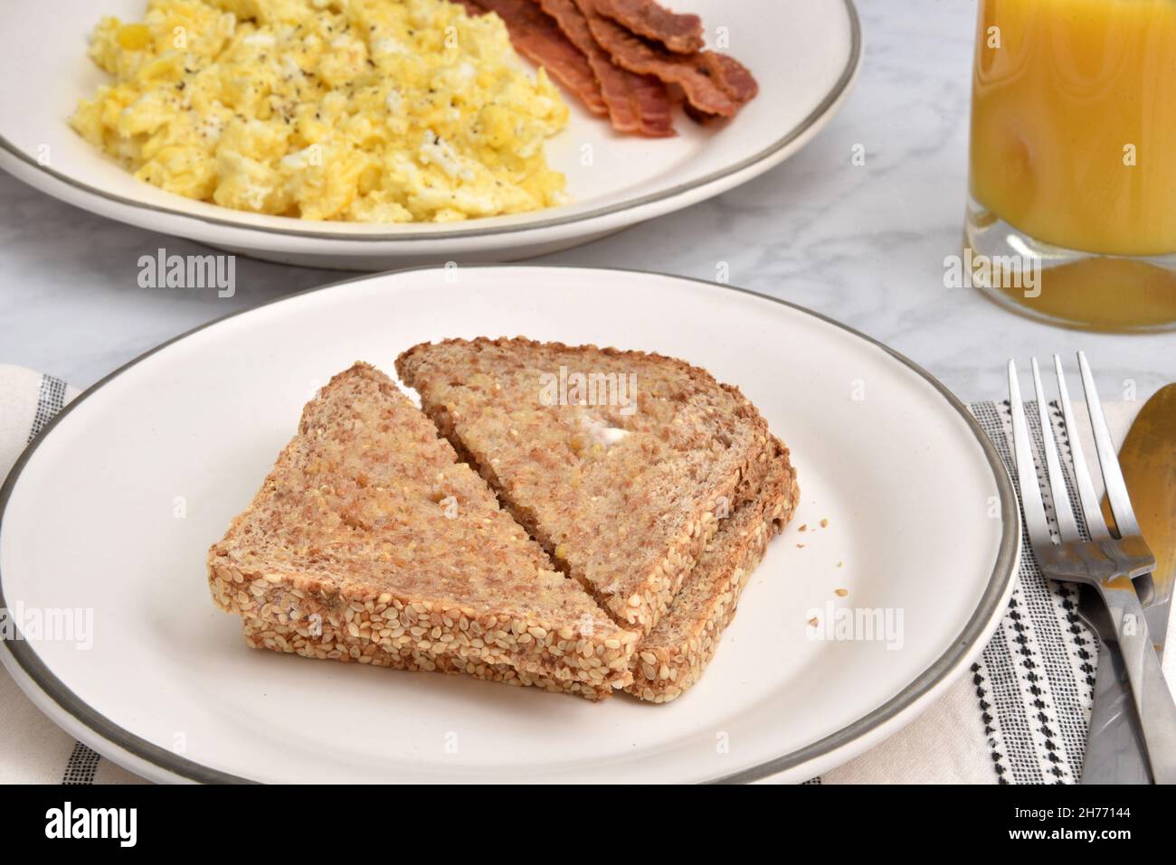 Hot buttered whole grain toast with sesame seeds and a bacon and egg breakfast Stock Photo