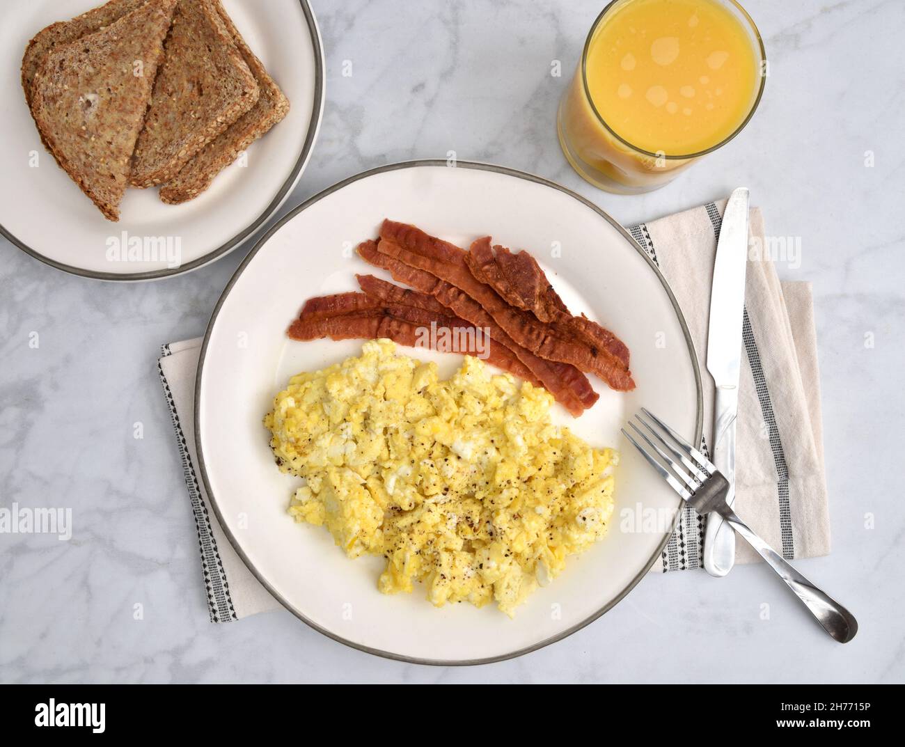 Overhead view of a plate of bacon and scrambled eggs with whole grain toast and a glass of orange juice Stock Photo