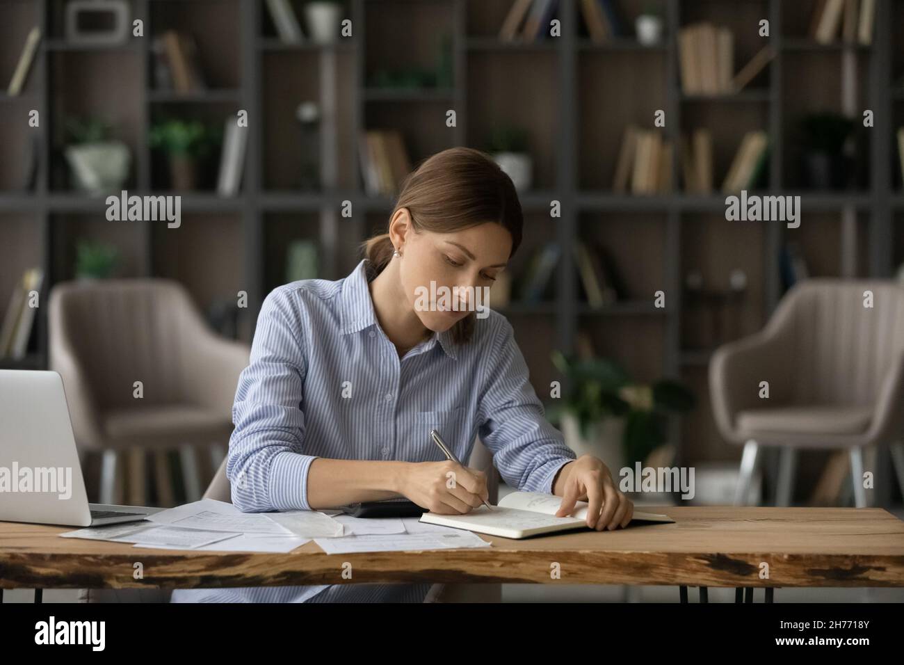Woman writing in diary, jotting to-do list seated at desk Stock Photo