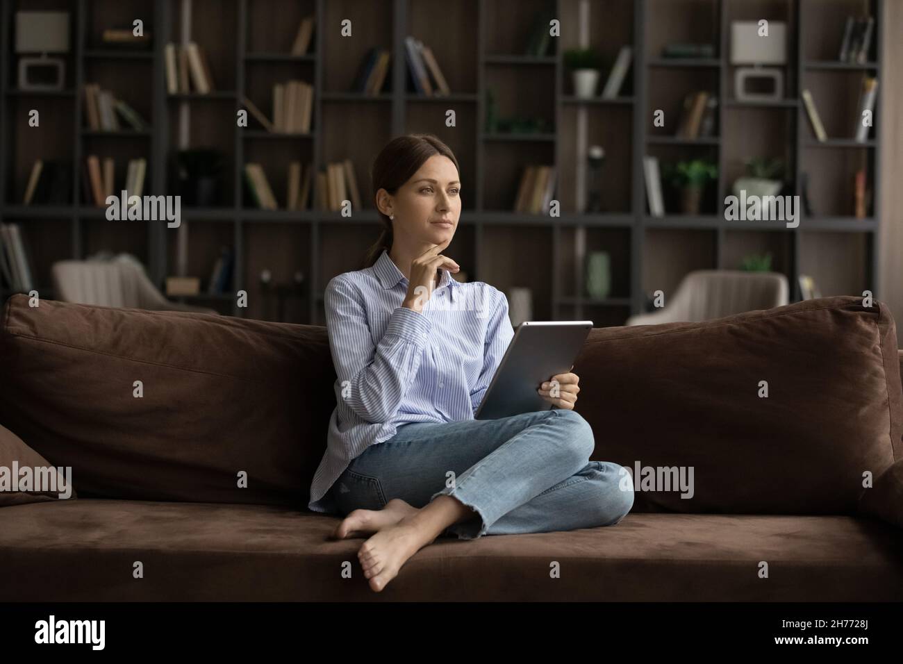Pensive woman sit on sofa with digital tablet Stock Photo