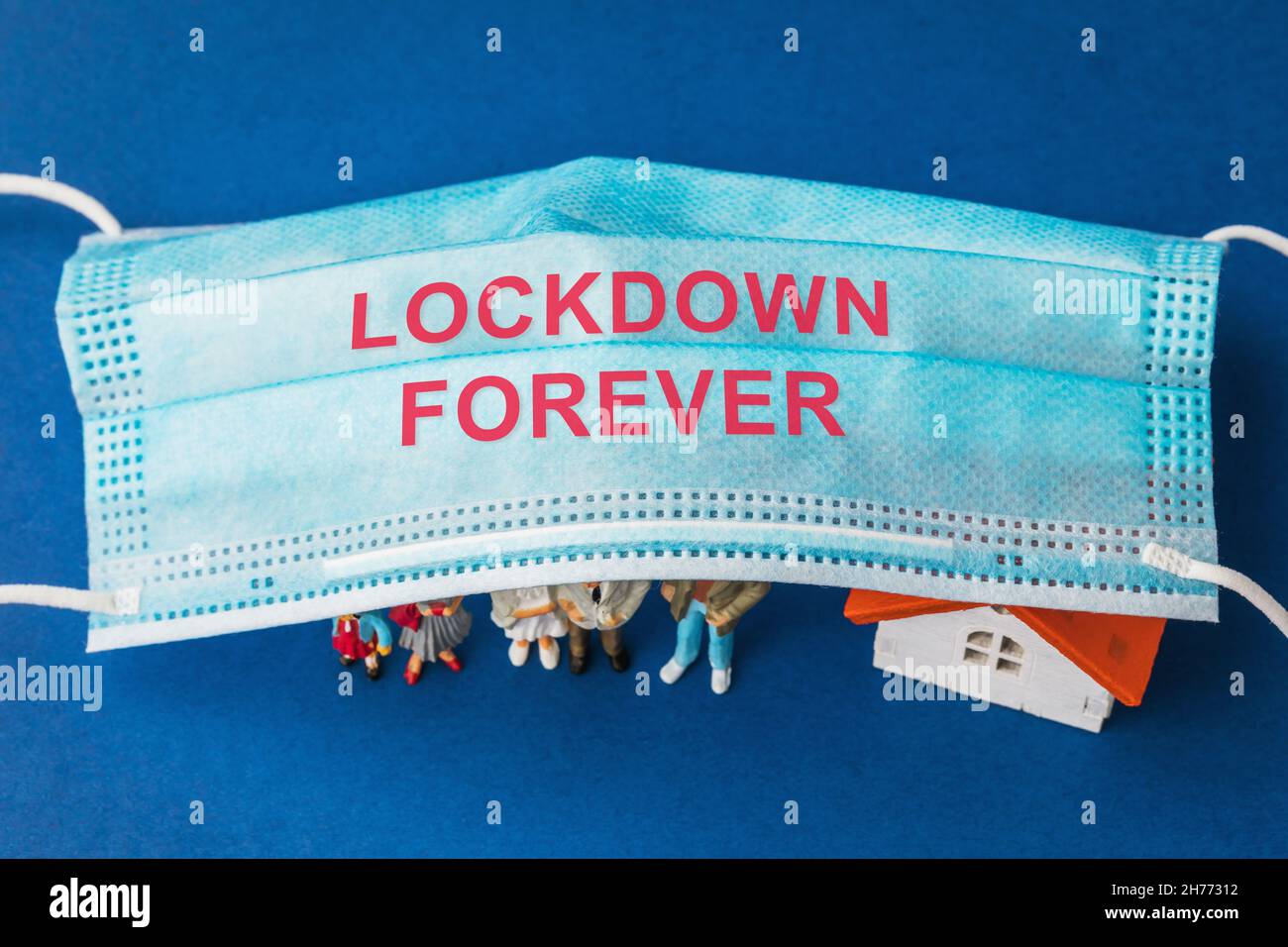 Medical mask with text and plastic toy men with a house under it, forever lockdown concept Stock Photo