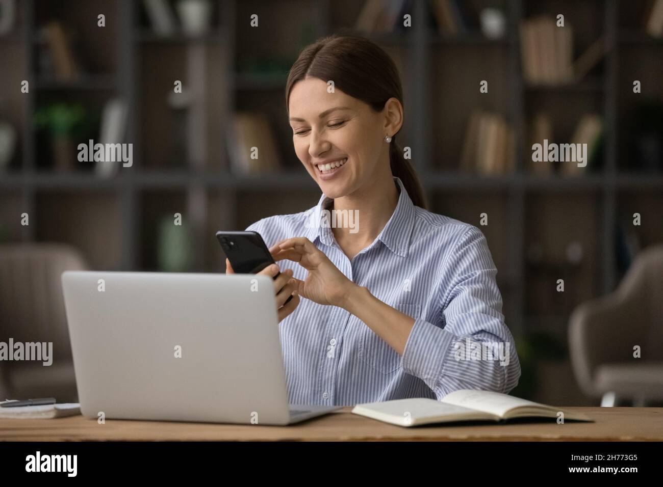 Happy business woman sit at workplace near laptop holding smartphone Stock Photo