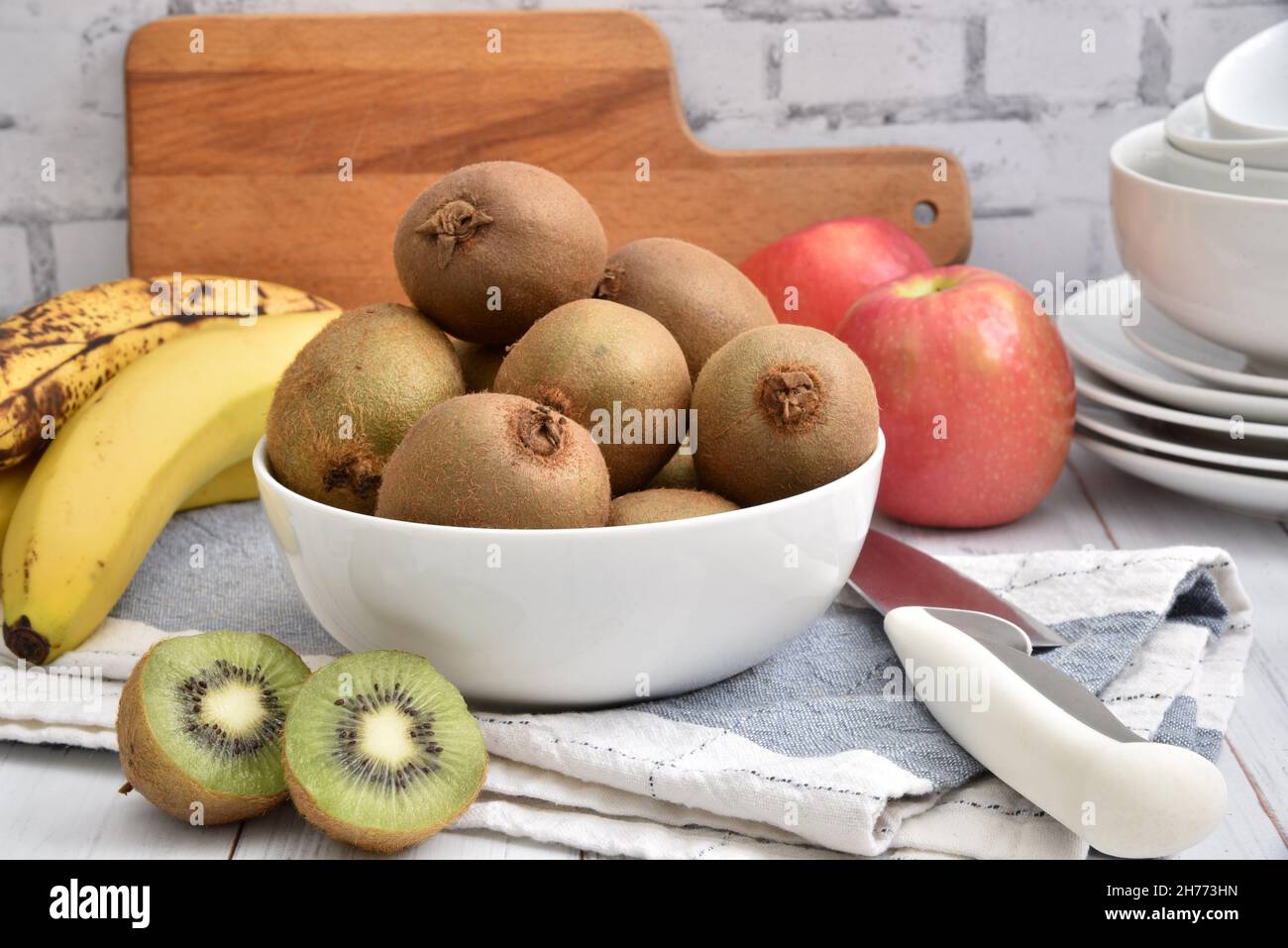 A bowl of kiwi fruit with bananas and apples on wooden kitchen counter Stock Photo