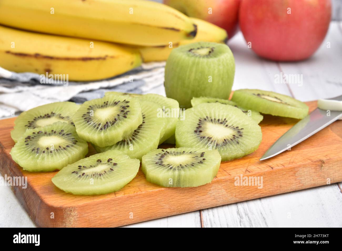 Fresh sliced kiwi on a cutting board with bananas and apples close up Stock Photo