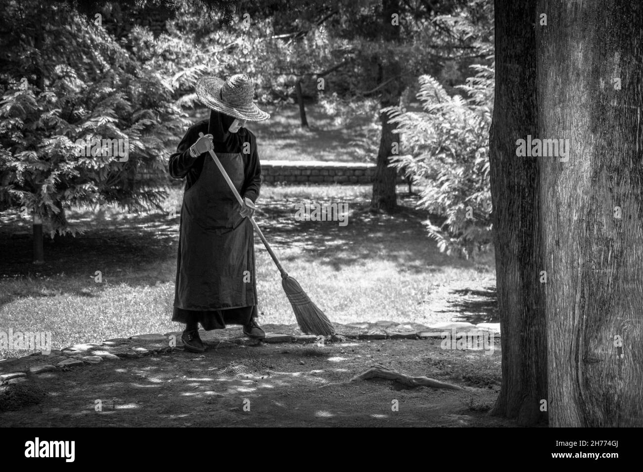 Diligent nun sweeping leaves off the patio in the orthodox Bodbe Monastery, Georgia. Black and white. Stock Photo