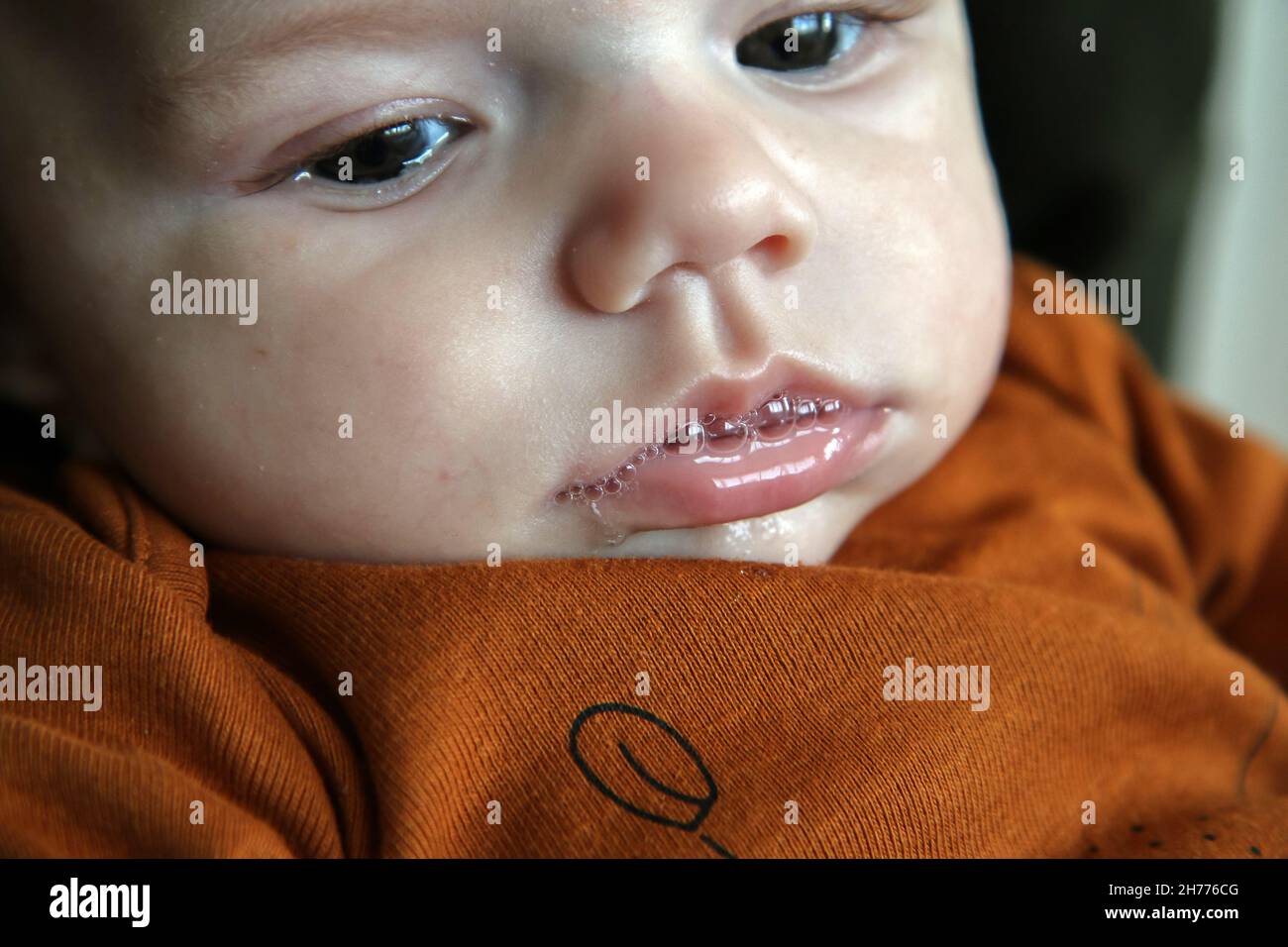 The detail of the baby having foam from the slaver on its mouth. Looking unhappy and absorbed in thoughts. Stock Photo