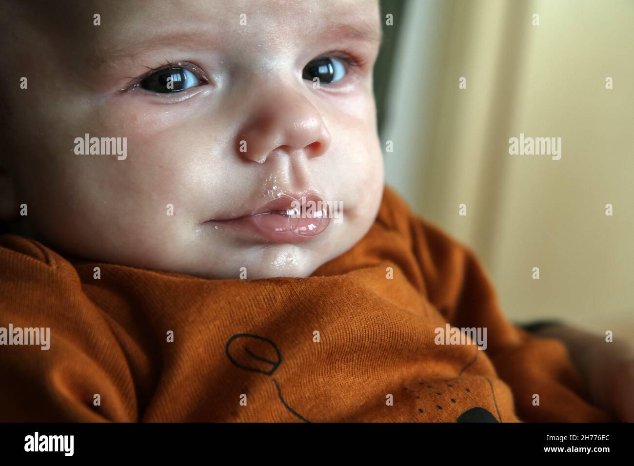 The detail of the baby having foam from the slaver on its mouth. Looking unhappy and absorbed in thoughts. Stock Photo