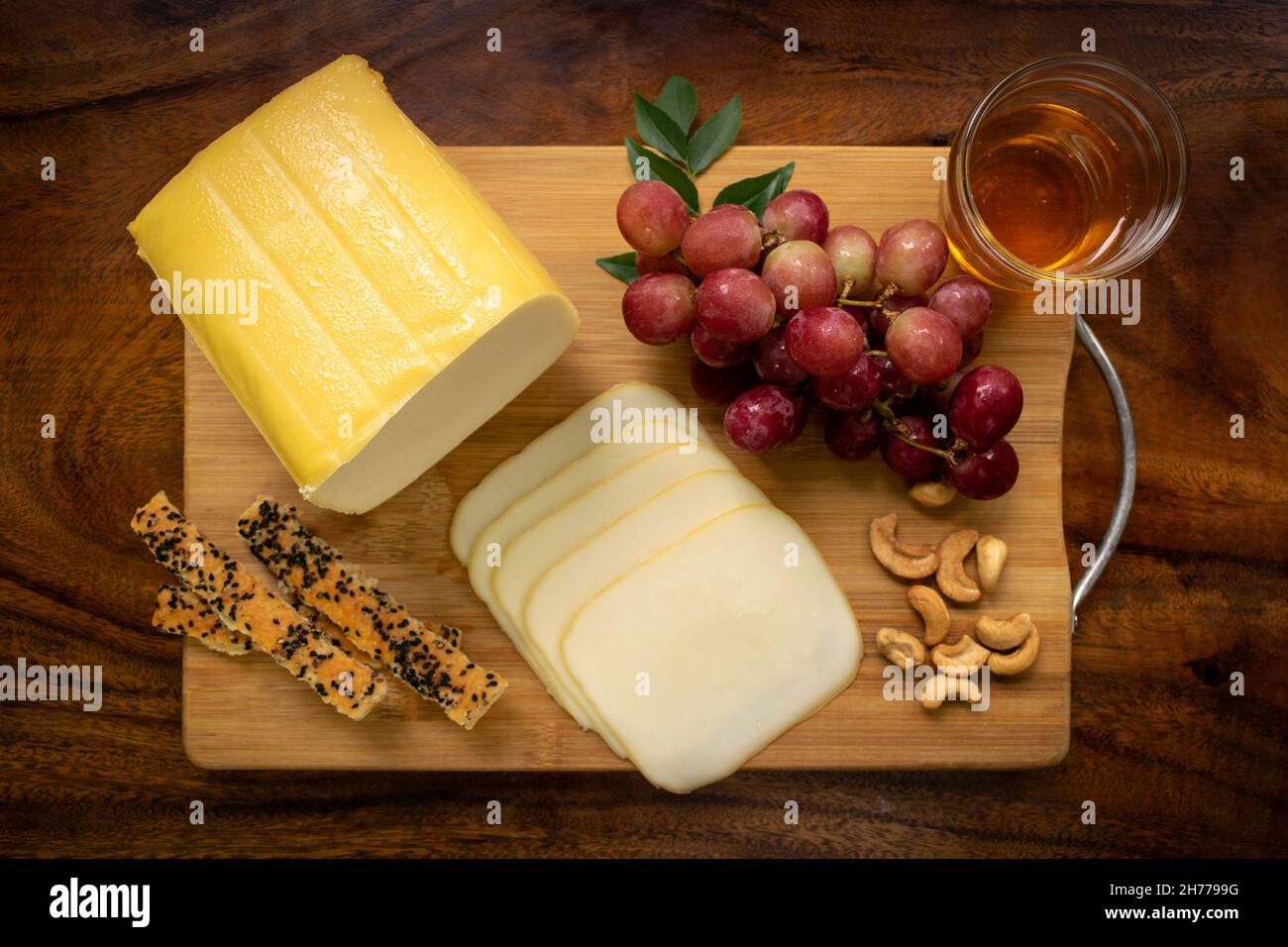 smoked mozzarella cheese block on wood board with grapes, cashew nuts, bread sticks and honey Stock Photo