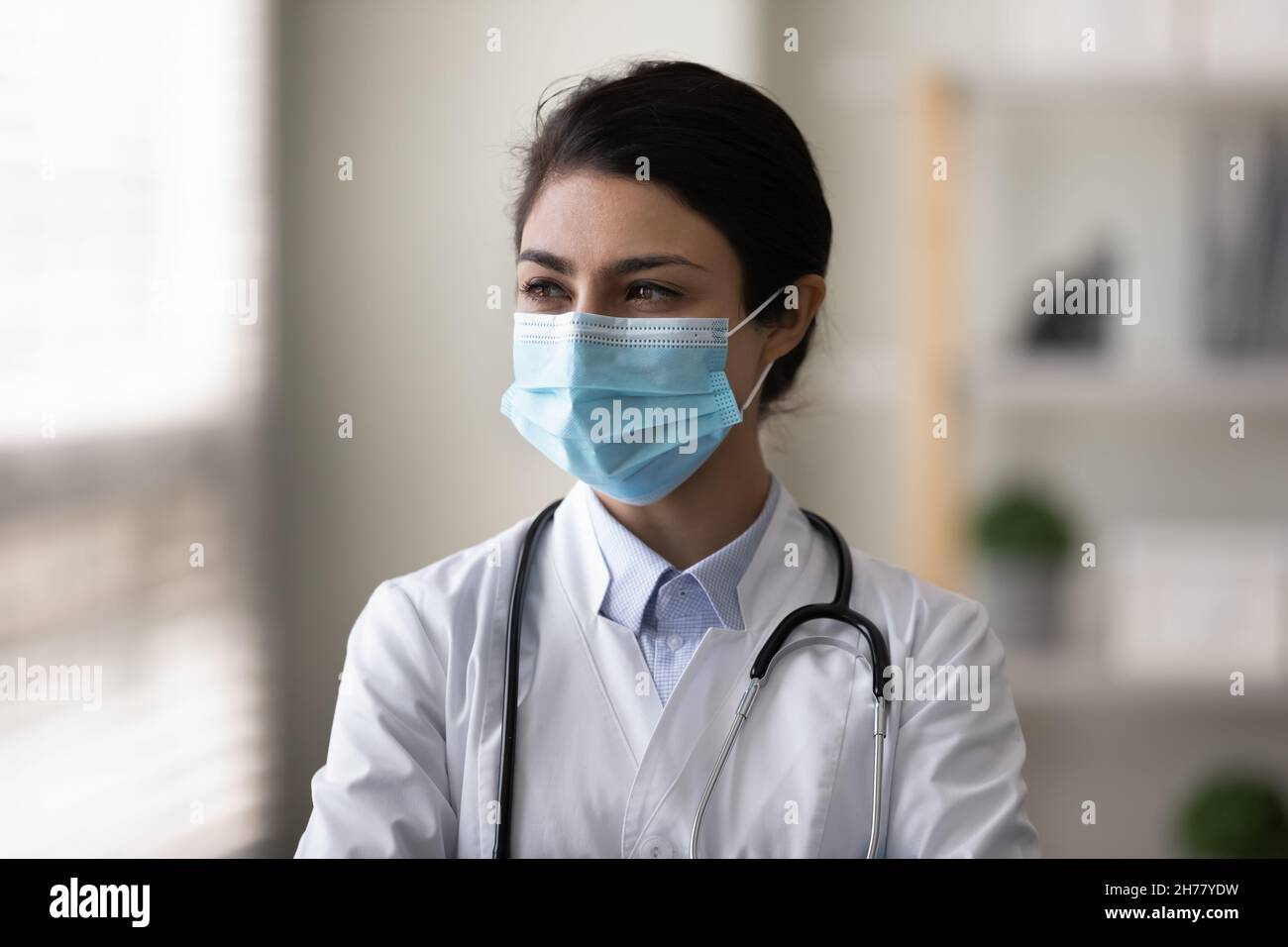 Head shot pensive Indian woman doctor in mask thinking Stock Photo