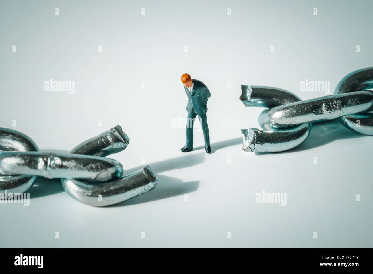 Macro photo of thoughtful businessman figurine standing between broken chain.  Sad and stressed miniature man close-up. Sad and stressed miniature man Stock Photo