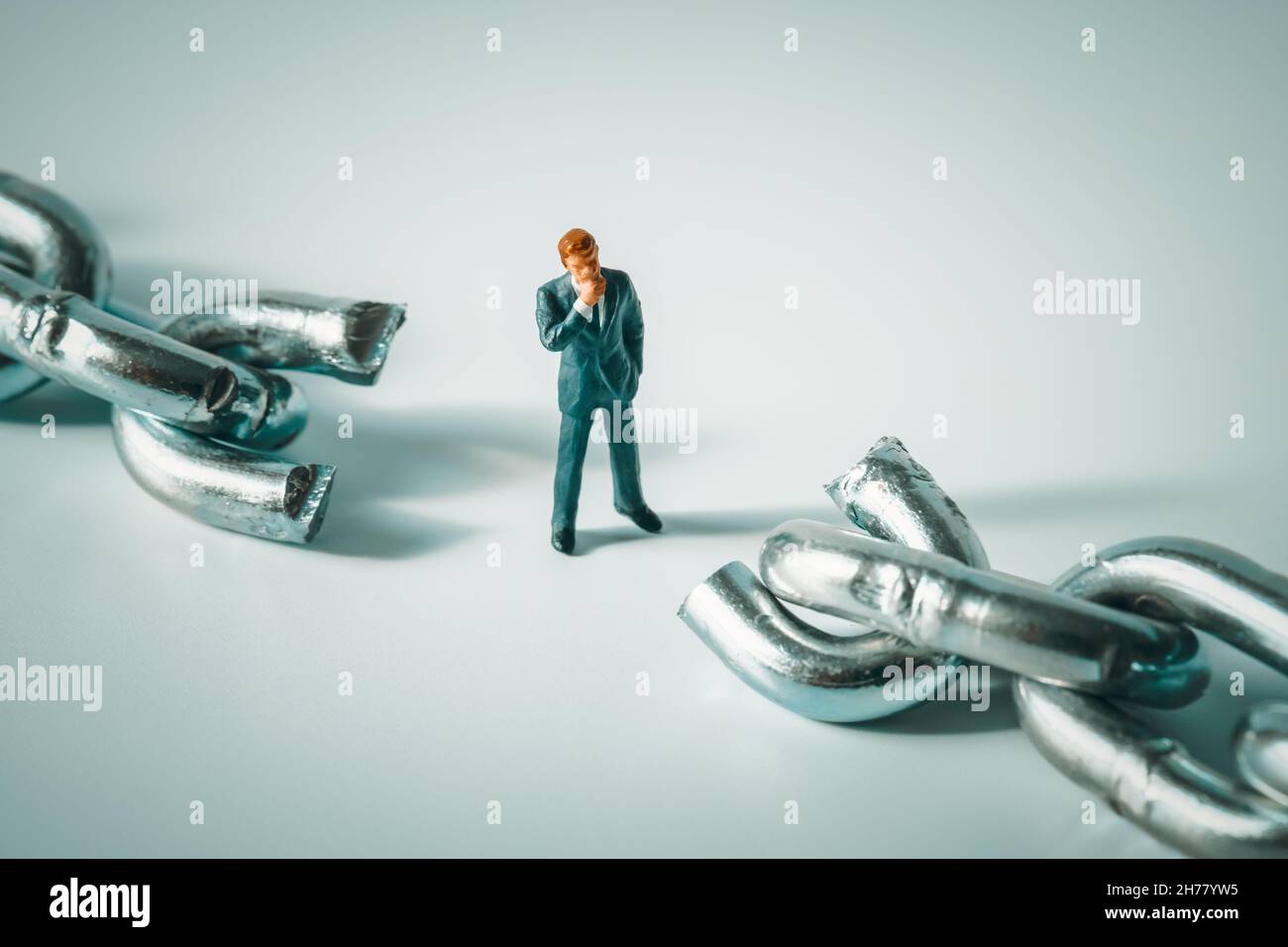 Macro photo of thoughtful businessman figurine standing between broken chain. Pondering miniature man close-up. Conflict, bankruptcy, indecision Stock Photo