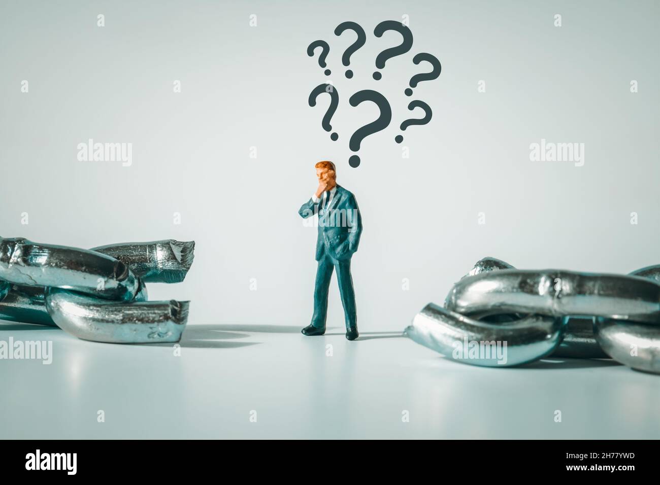 Macro photo of thoughtful businessman figurine standing between broken chain. Question marks above the pondering miniature man.  Conflict, bankruptcy, Stock Photo