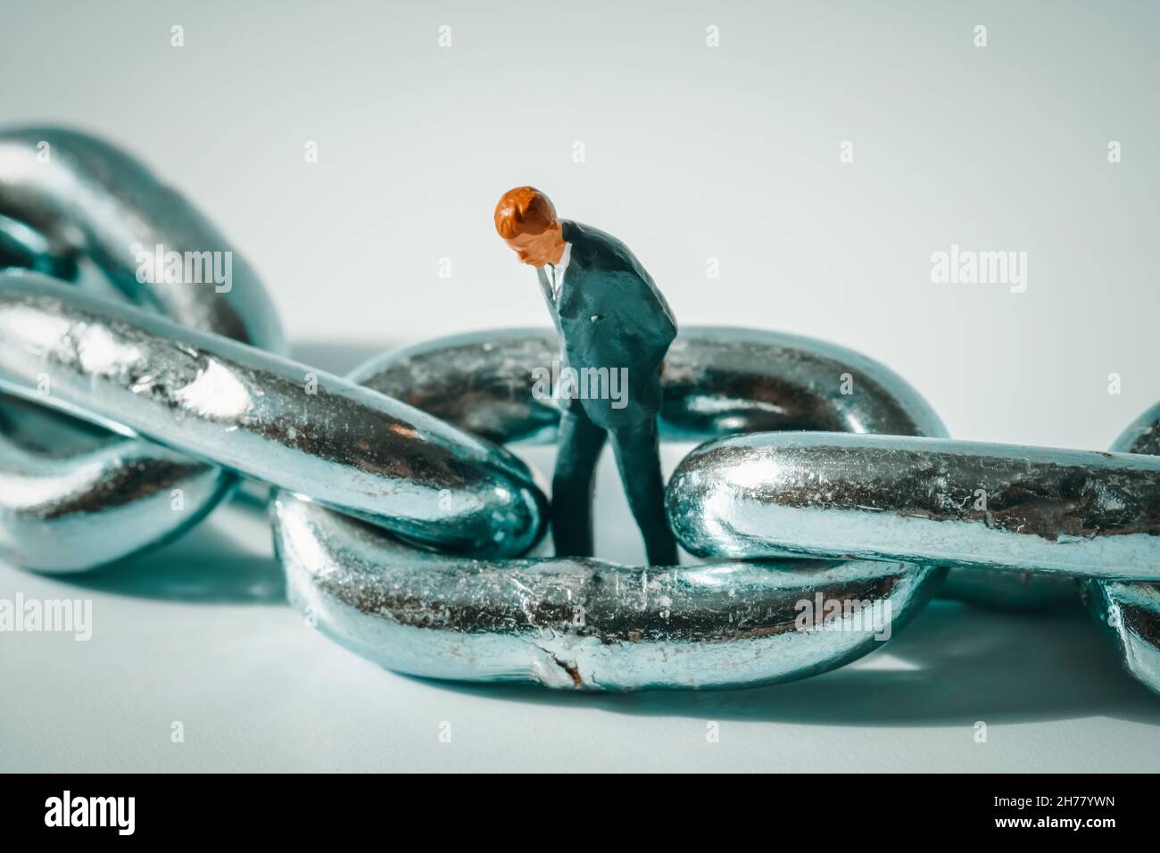 Macro photo of thoughtful businessman figurine standing in a ring of chain. Business failure, bankruptcy, unemployment concept. Stressed unemployed Stock Photo