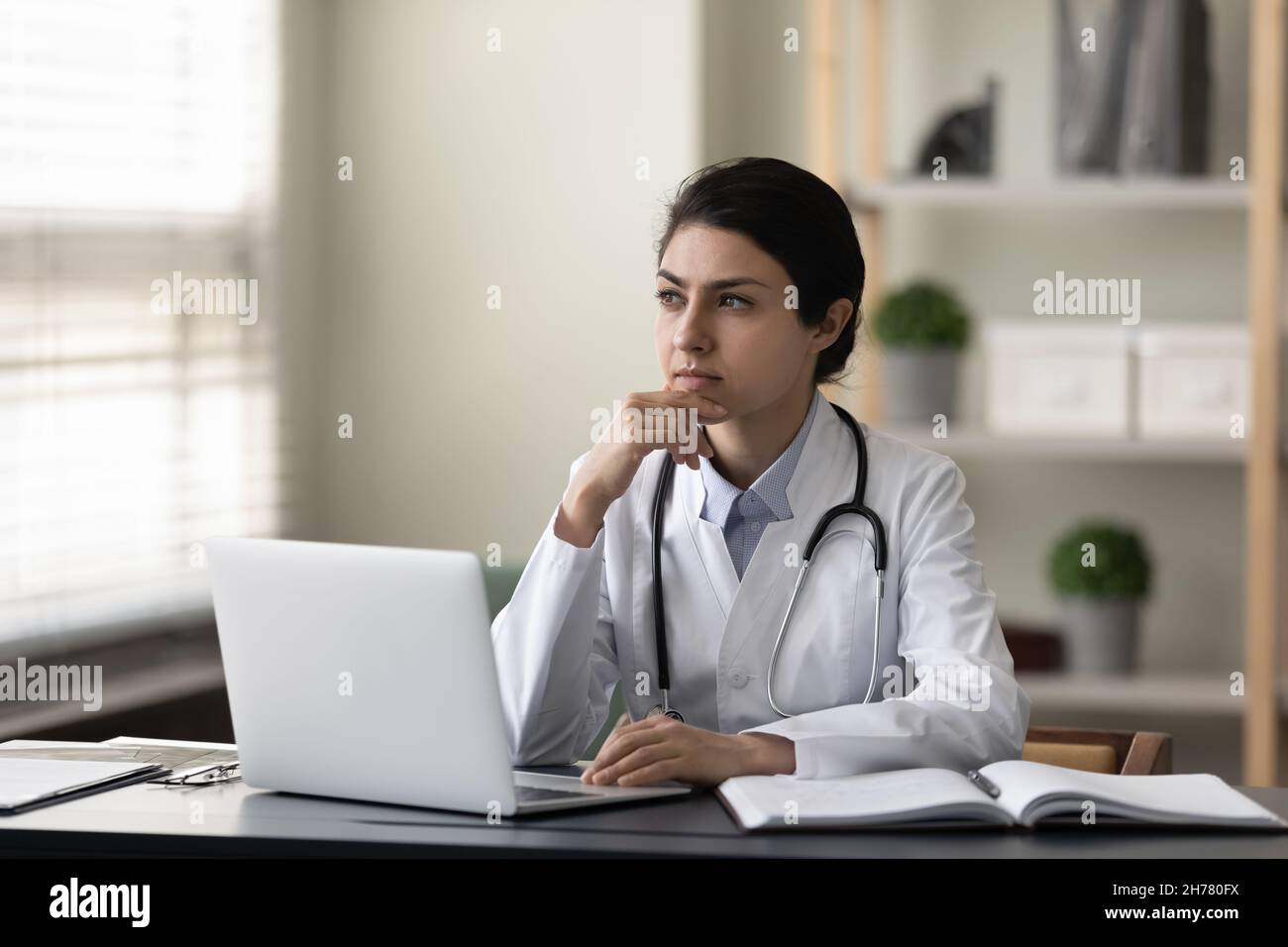 Thoughtful serious Indian female doctor physician sitting at work desk Stock Photo