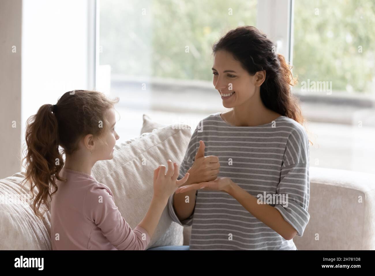 Smiling caring mother teaching disabled daughter, learning sign gesture