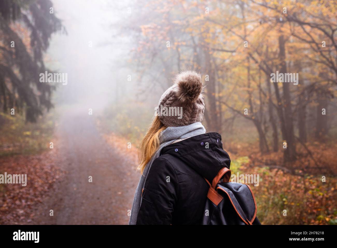 Woman with backpack and knit hat hiking in foggy forest. Tourist looking for adventure in nature. Mystery woodland Stock Photo