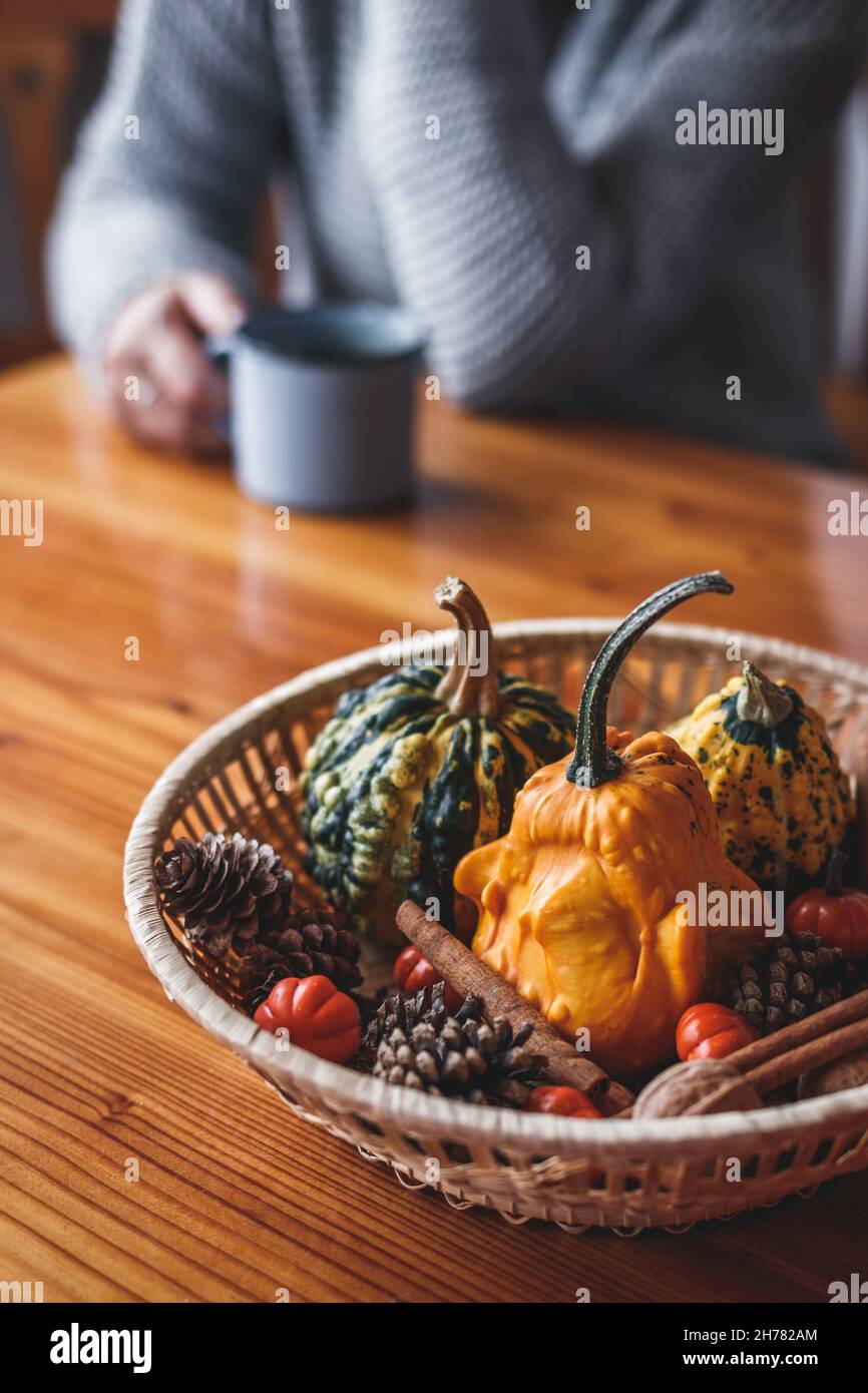 Autumn decoration with pumpkins on wooden table. Defocused woman wearing knitted sweater enjoying coffee drink Stock Photo
