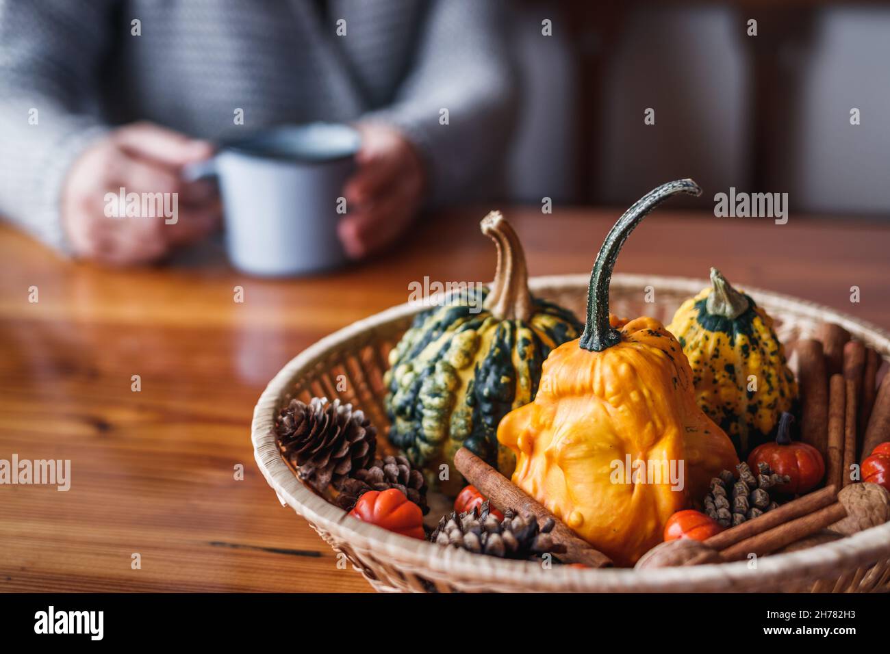 Autumn decoration with pumpkins on wooden table. Defocused woman wearing knitted sweater drinking hot coffee Stock Photo