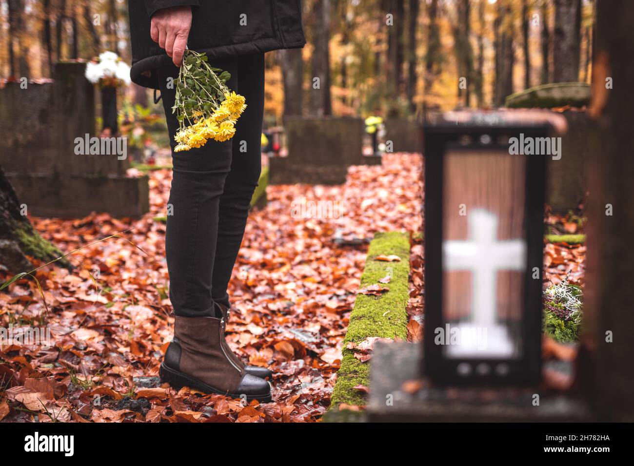 Mourning woman holding flowers in hands and standing at grave in cemetery. Sadness and grief during funeral Stock Photo